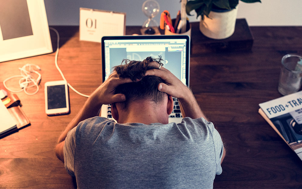 Homem trabalhando em frente ao computador, segurando a cabeça, sentindo-se esgotado, com risco de desenvolver burnout.