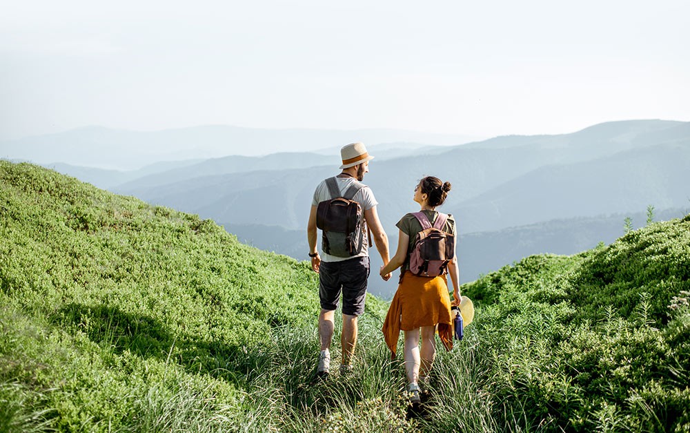 Viagem de casal, onde ambos exploram uma região serrana enquanto caminham de mãos dadas e mochila nas costas