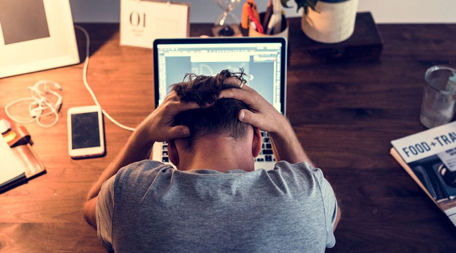 Homem trabalhando em frente ao computador, segurando a cabeça, sentindo-se esgotado, com risco de desenvolver burnout.