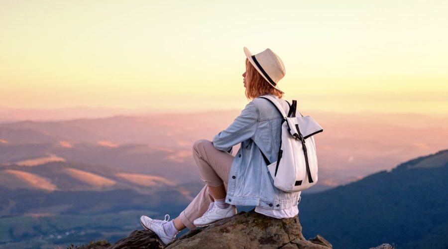 Mulher com uma mochila nas costas no topo de uma montana no nascer do sol.