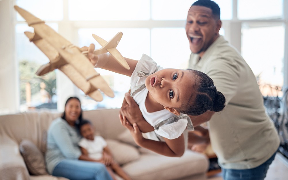 Pai e filha brincando com avião, ambos se divertindo, criando uma memória afetiva