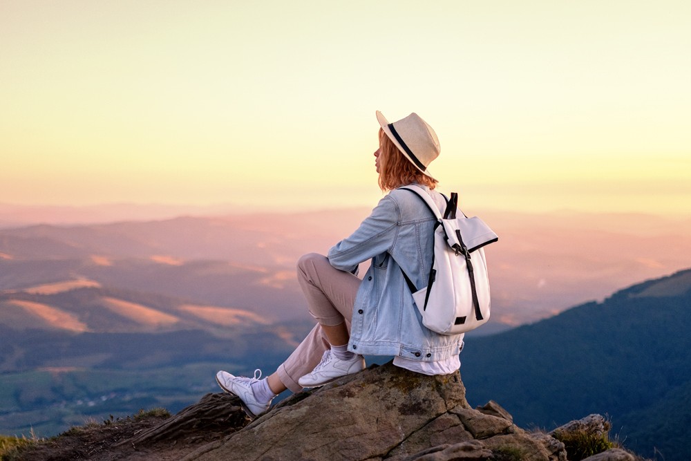 Mulher com uma mochila nas costas no topo de uma montana no nascer do sol.